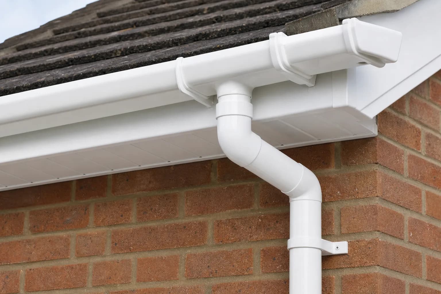 White uPVC guttering, fascia and soffit along the eaves of a brick house with a downpipe