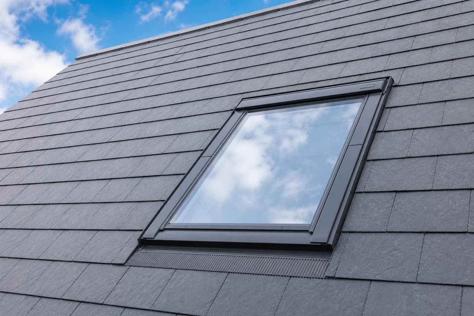 A Velux roof window set flush into a grey slate pitched roof with neat flashing